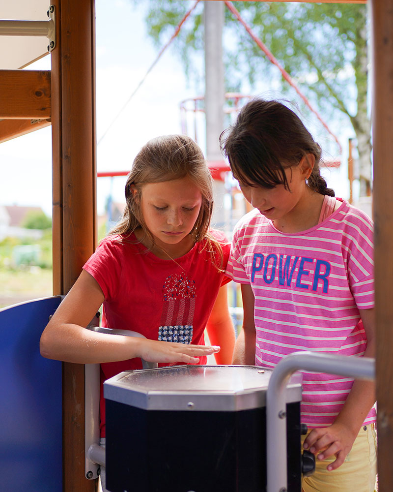 Two young girls play on a multi play unit, there are musical drums underneath one of the units.